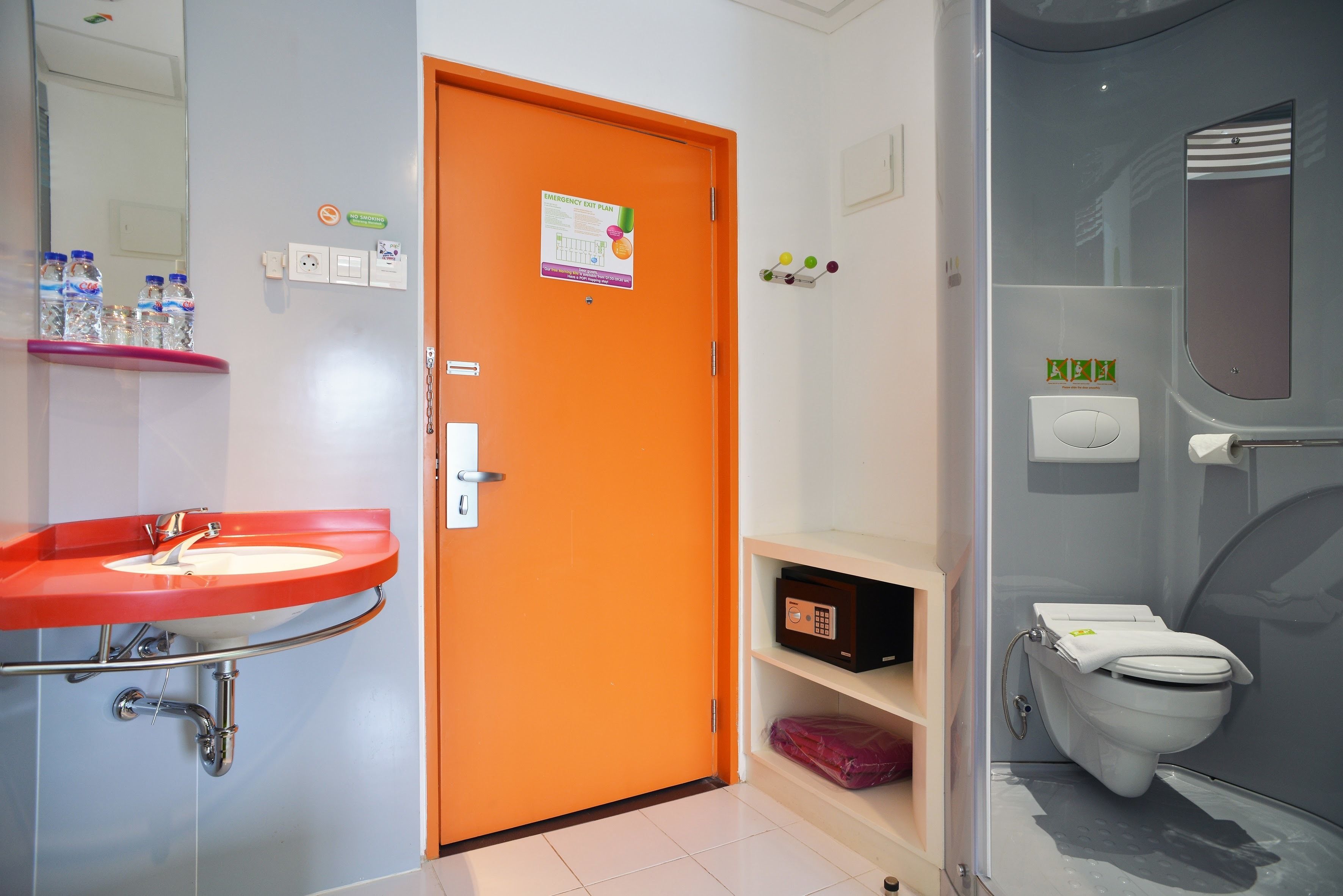 A bathroom with a red sink, an orange door, a white toilet, and a glass shower enclosure.