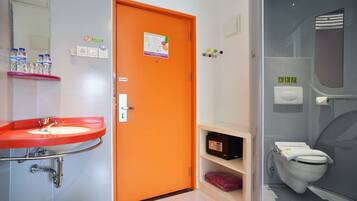 A bathroom with a red sink, an orange door, a white toilet, and a glass shower enclosure.