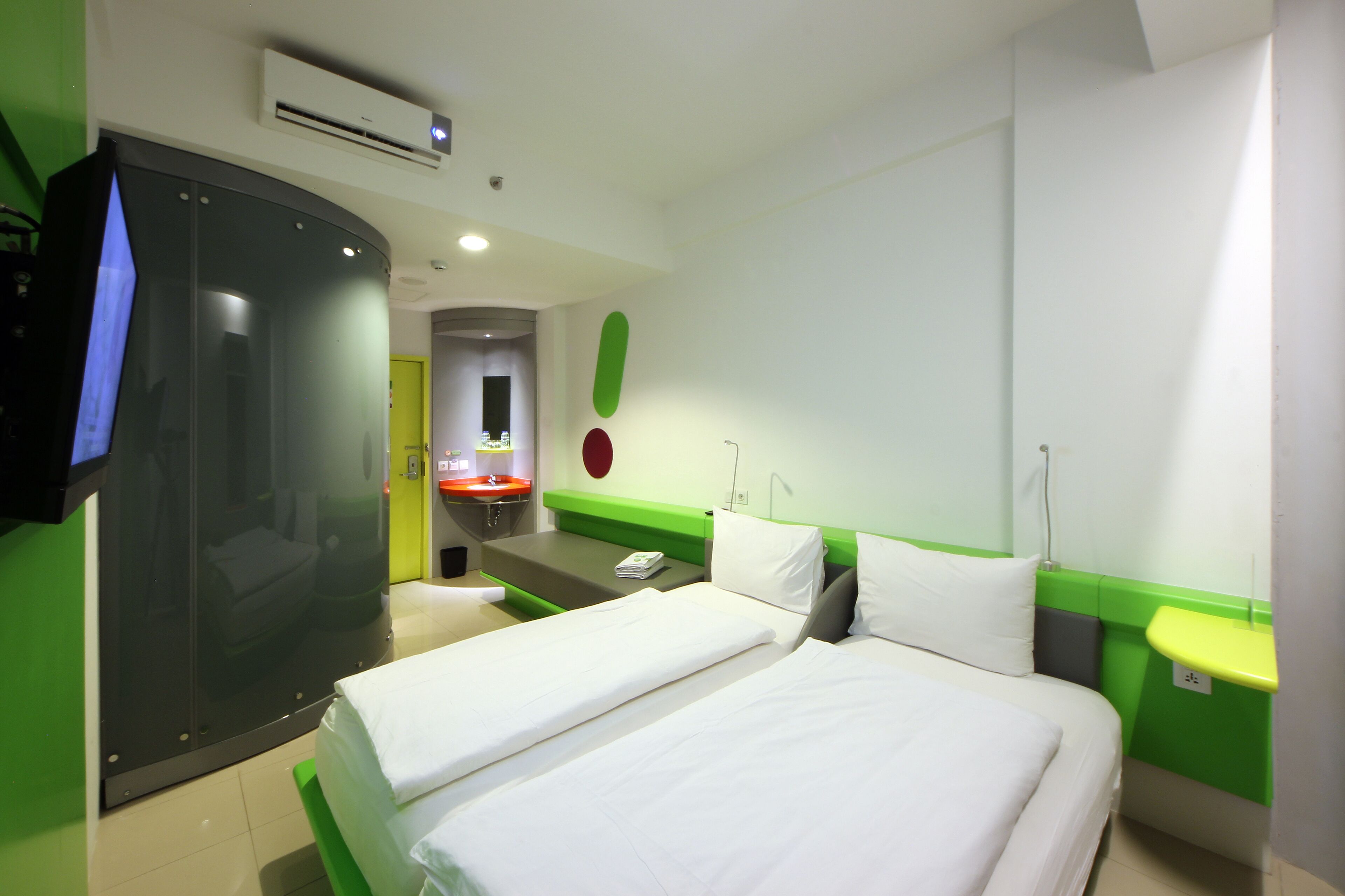 Een hotelkamer met twee bedden, een groene accentmuur, een wastafel en een spiegel.
