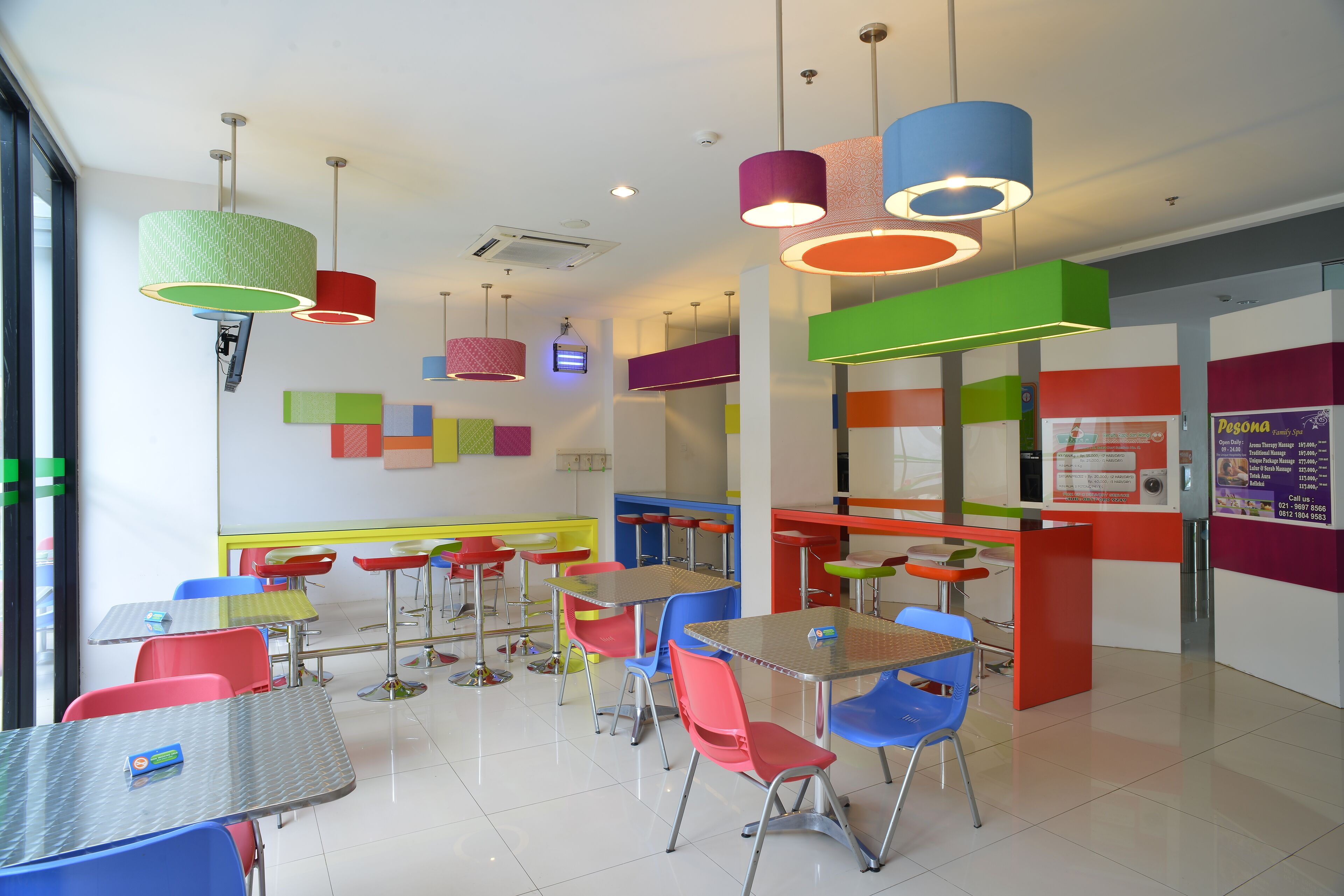 A brightly lit cafeteria with colorful chairs and tables, a whiteboard, and a menu board.