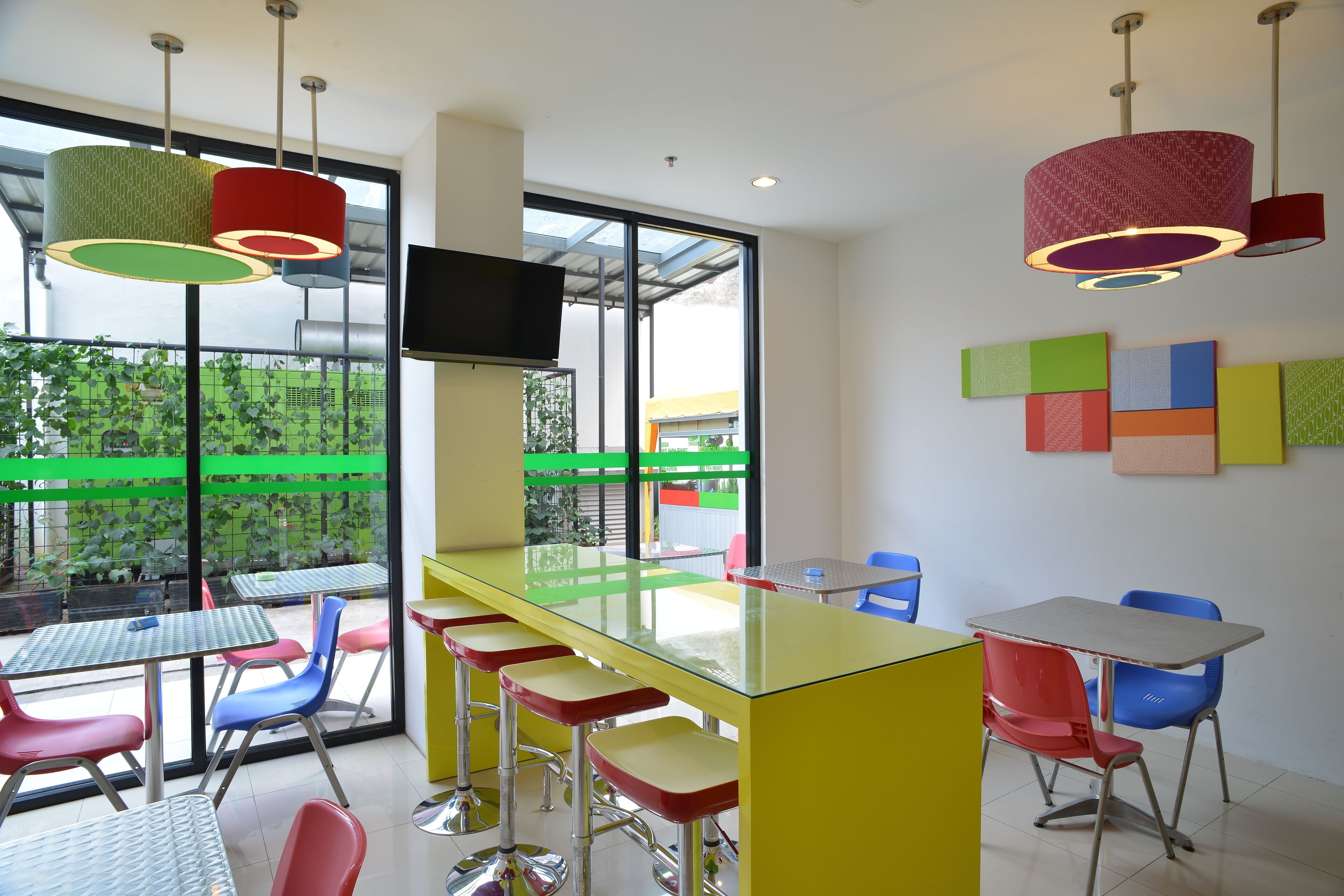 A brightly lit indoor space with a long bar area, multiple chairs, and a television mounted on the wall.