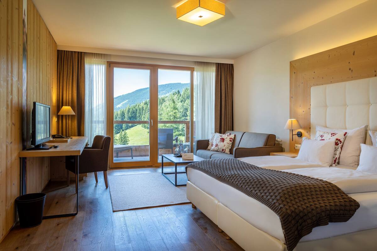 A hotel room with a bed, a desk, a chair, a TV, and a view of the outdoors.
