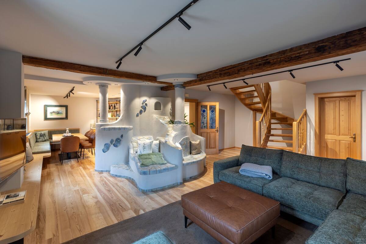 A spacious living area with a wooden staircase, a sofa, a coffee table, and a unique white, stone-like seating area.