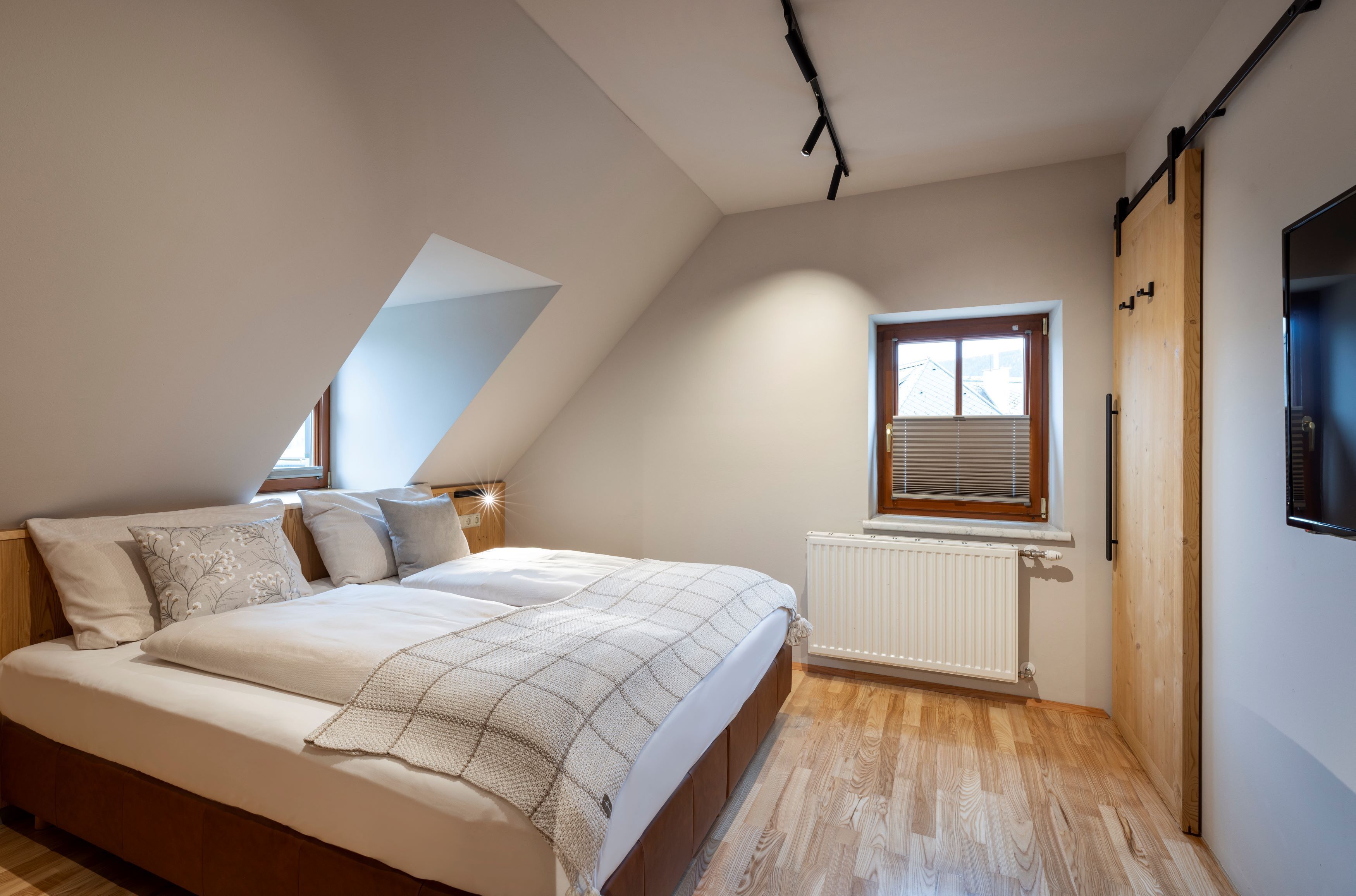 A bedroom with a bed, a window with blinds, a radiator, and a wooden door.