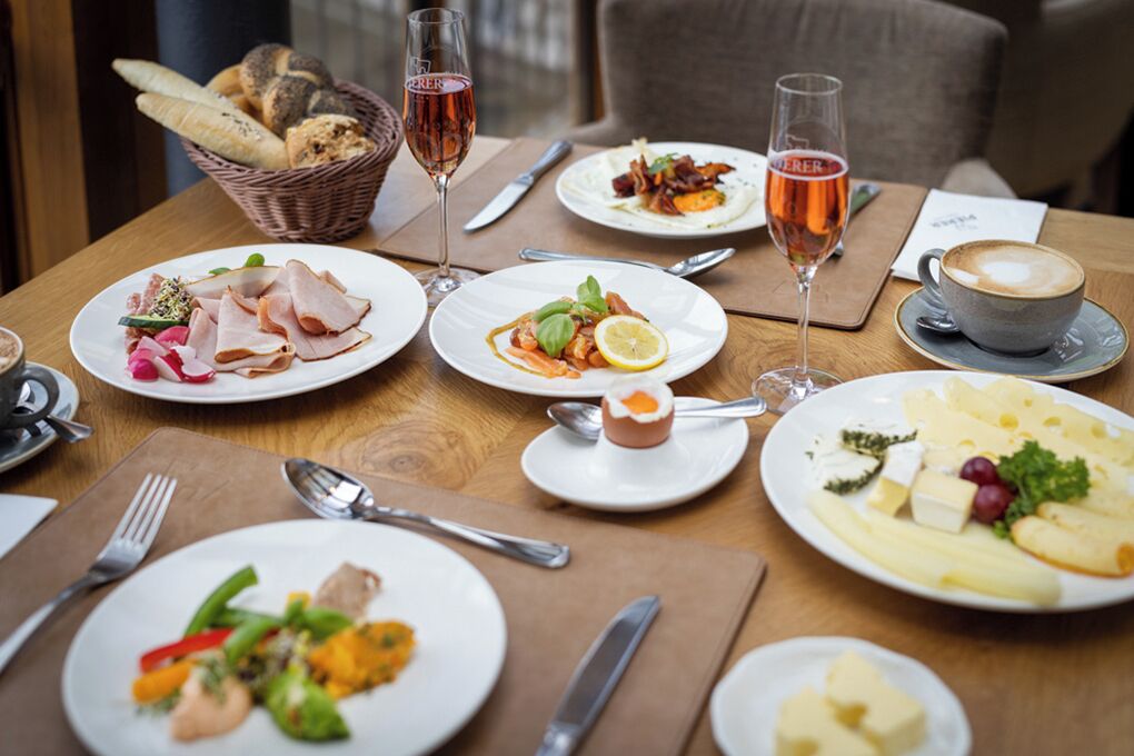 A dining table with various plates of food, glasses of wine, and cutlery.