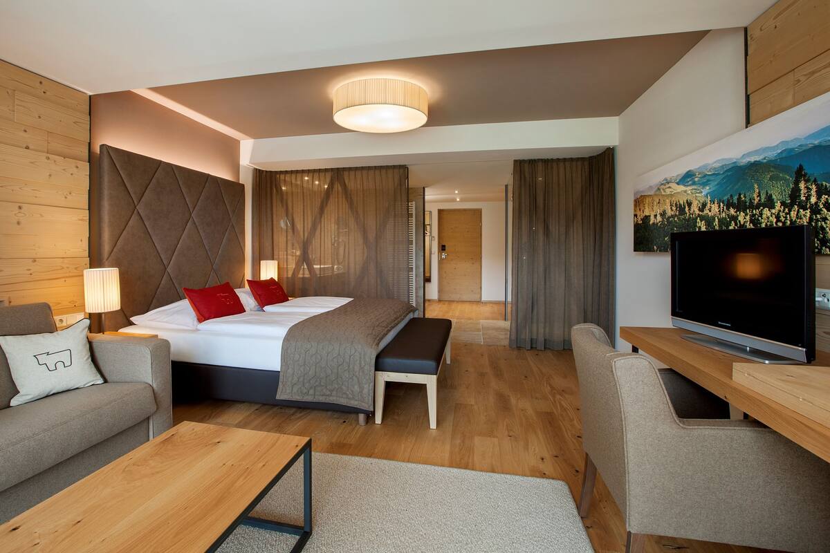 A modern hotel room with a bed, a sofa, a TV, and a painting on the wall.