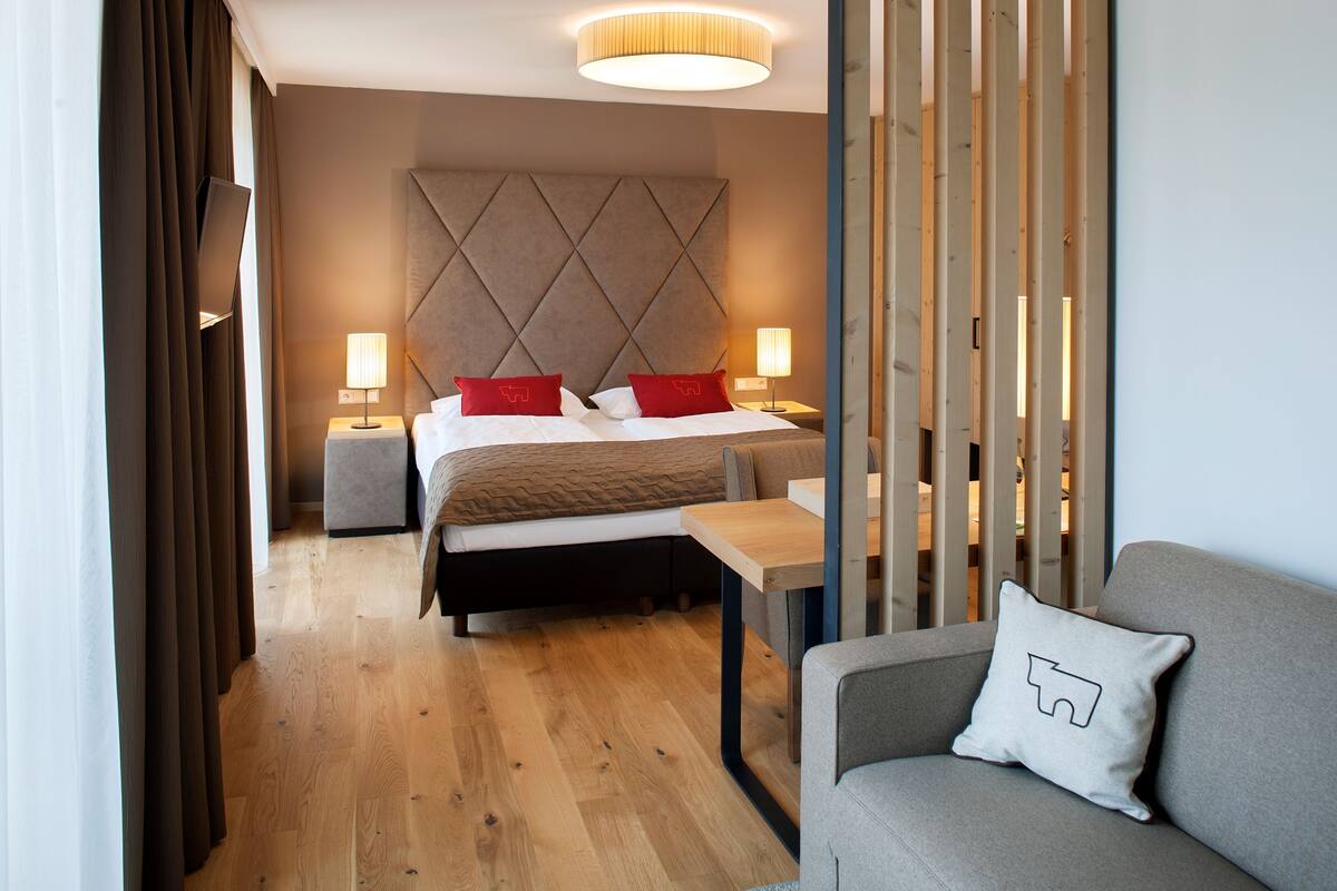 A modern hotel room with a bed, bedside tables, a sofa, and a wooden partition.