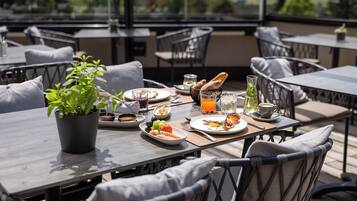 An outdoor dining area with multiple tables and chairs, a potted plant, and various breakfast items.
