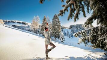 A person performing a yoga pose in a snowy outdoor setting with snow-covered trees and a clear blue sky.
