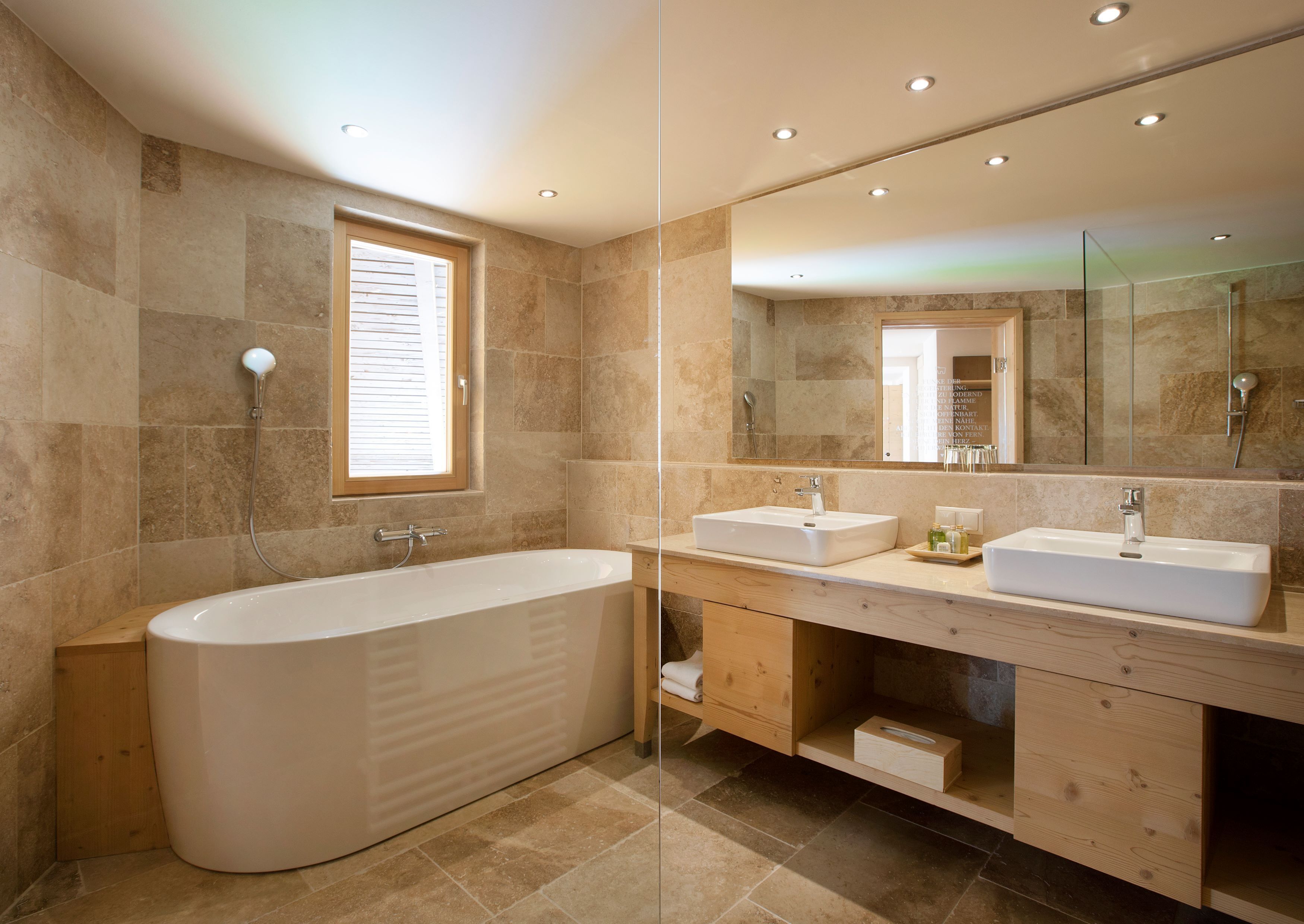 A modern bathroom with a freestanding bathtub, two sinks, and a large mirror.