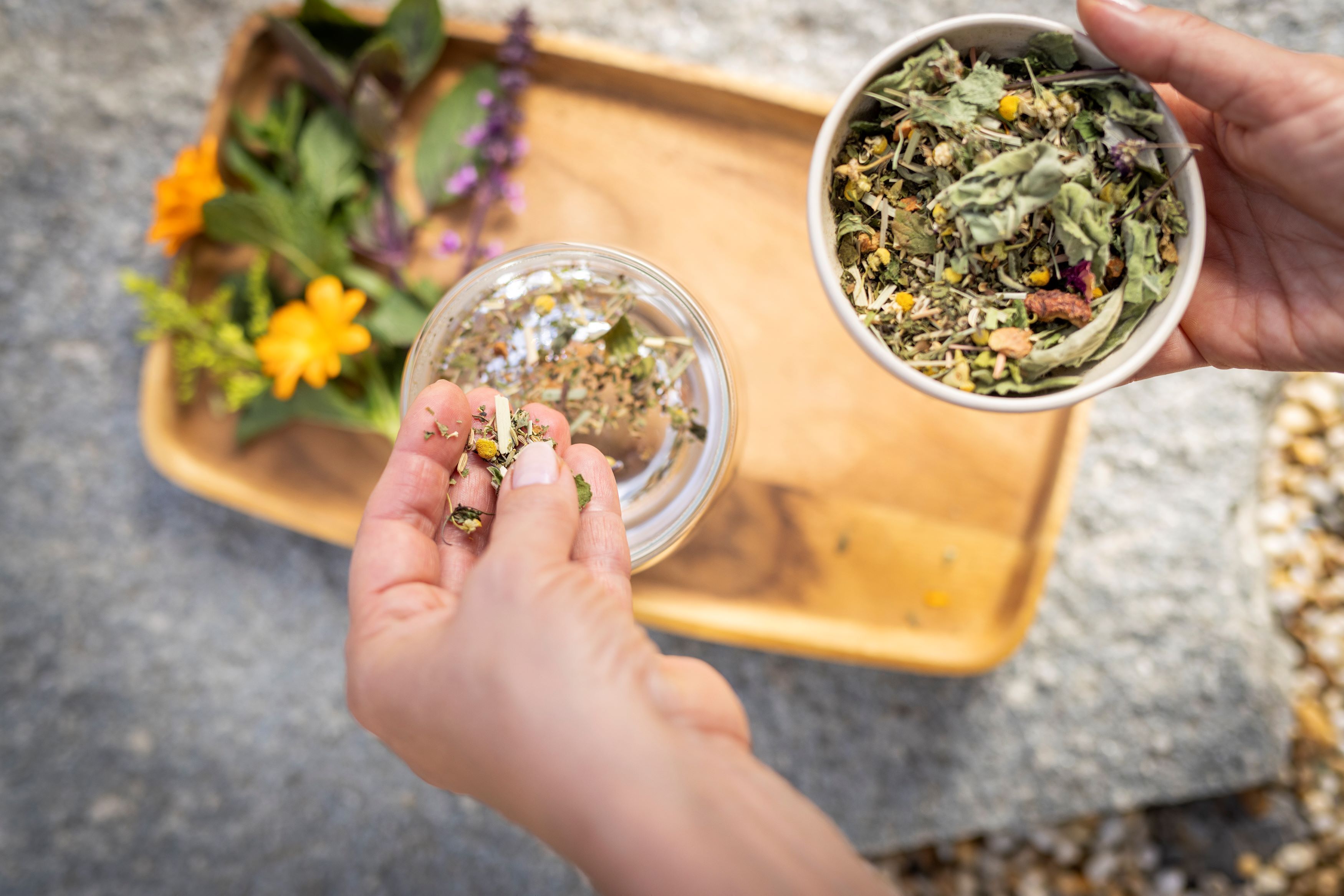 Two hands holding a small glass jar and a bowl of dried herbs.