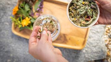 Two hands holding a small glass jar and a bowl of dried herbs.