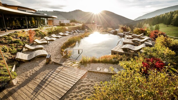 Un espace bien-être comprenant un bain à remous, des chaises longues et une terrasse en bois donnant sur un lac.