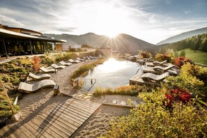 A spa area with a hot tub, lounge chairs, and a wooden deck overlooking a lake. - Almwellness Hotel Pierer (Fladnitz an der Teichalm)