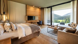 Une chambre d’hôtel moderne dotée d’un grand lit, d’un bureau, d’une télévision et d’un balcon offrant une vue panoramique sur les montagnes.