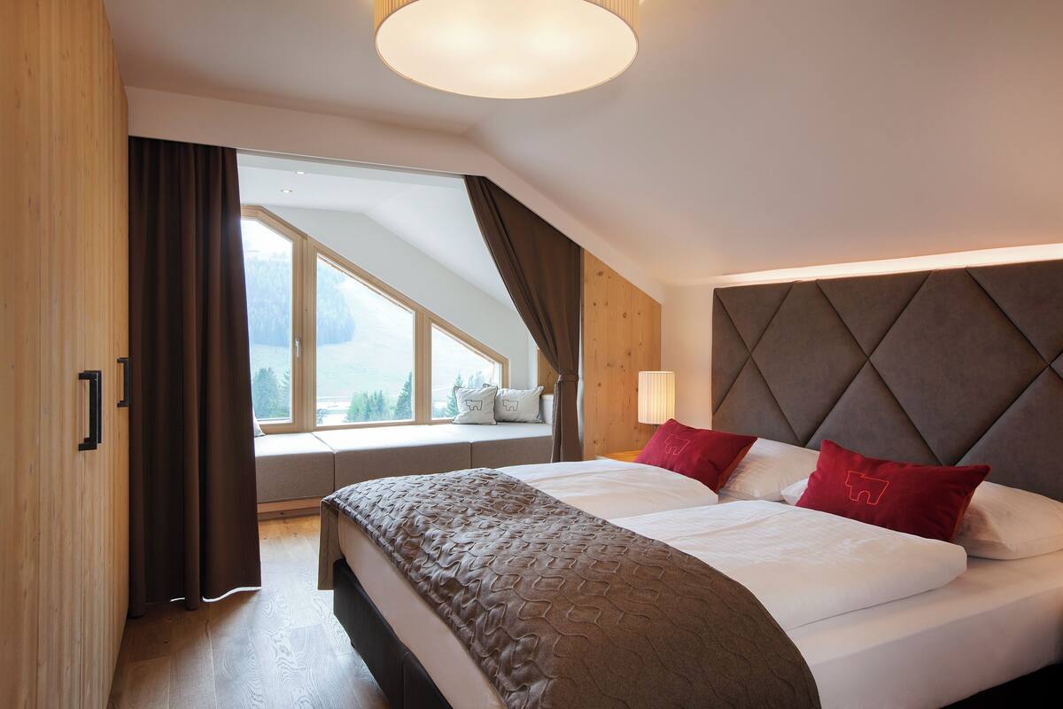 A bedroom with a large bed, a window seat, and a view of the outdoors.