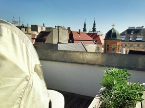 Une terrasse sur le toit offrant une vue sur les bâtiments environnants, notamment une église dotée d’un dôme vert et de flèches.