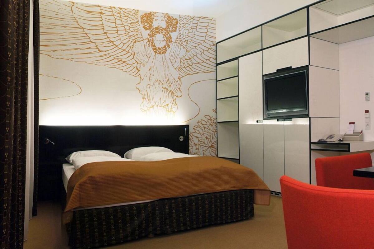 A hotel room with a large bed, a TV, a desk, and a red chair.