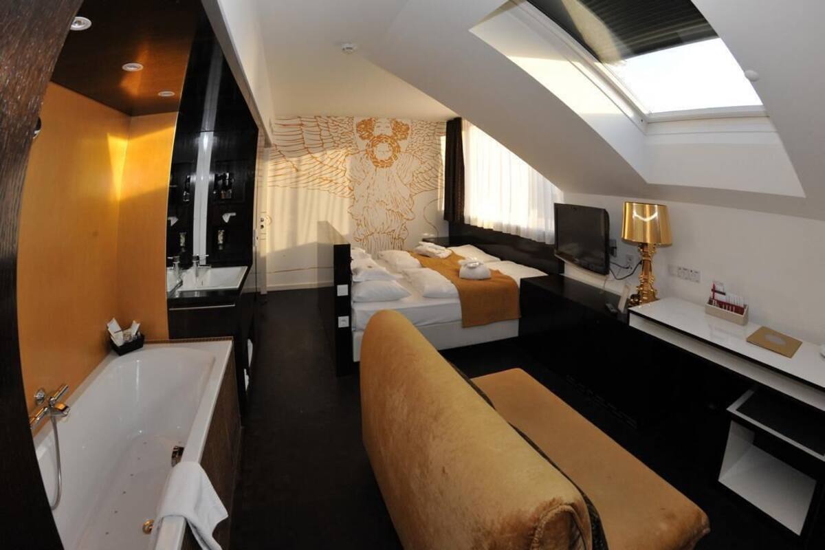 A modern hotel room with a skylight, a large bed, a desk, a TV, and a bathroom with a bathtub and shower.