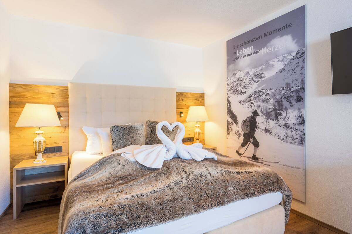 A hotel room with a bed, two bedside lamps, a nightstand, and a poster on the wall.