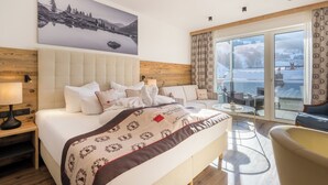A hotel room with a large bed, a sofa, a balcony with a view of a snowy landscape. - Hotel Alpenkönigin Alpine Luxury   (See)