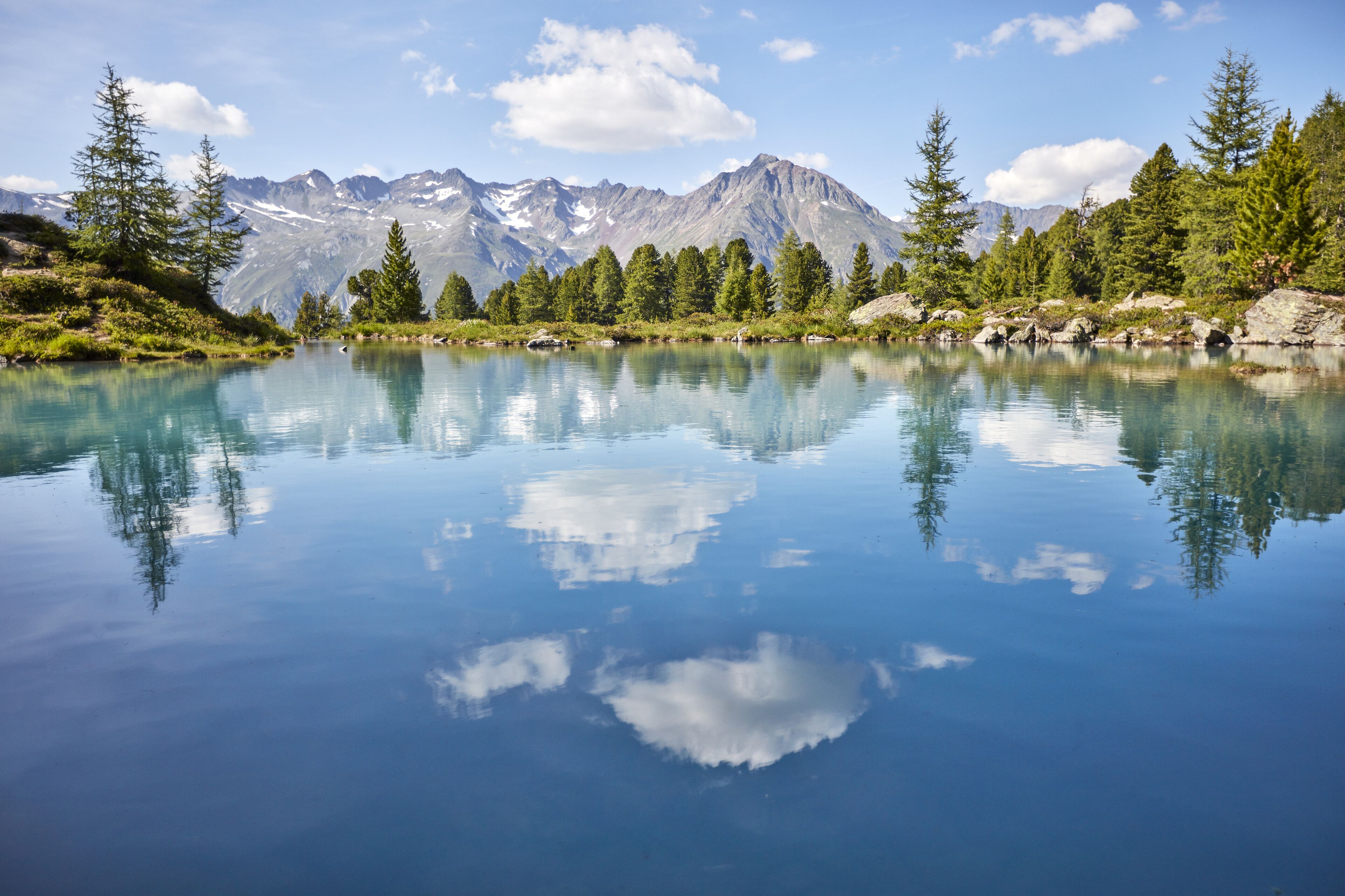 Un lago tranquilo con reflejos de árboles y montañas, rodeado de exuberante vegetación y terreno rocoso.