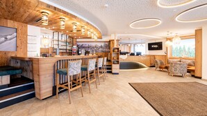 A modern bar area with wooden accents, bar stools, and a seating area with cushioned chairs. - Hotel Alpenkönigin Alpine Luxury   (See)