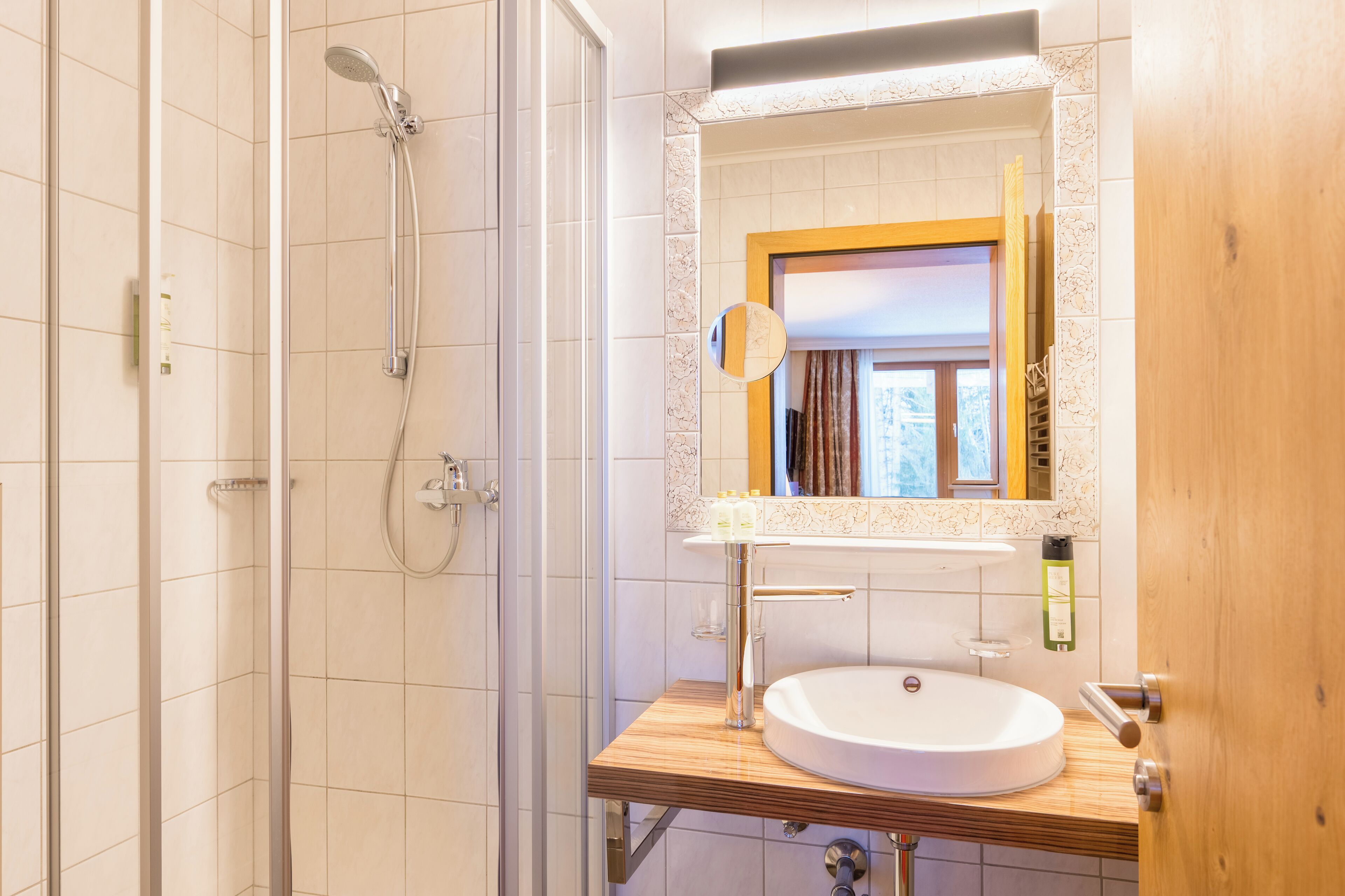 A bathroom with a wooden vanity, a white sink, and a glass shower enclosure.