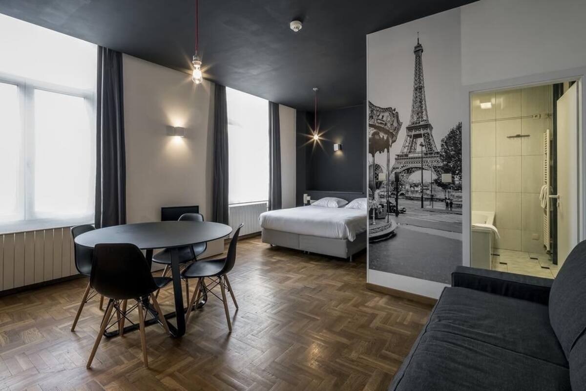 Una habitación de hotel moderna con cama, una mesa de comedor con sillas, un sofá y un ventanal grande.