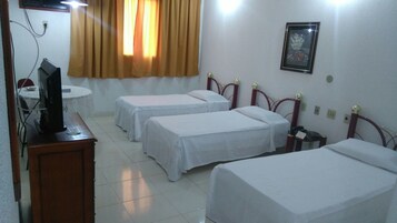 A hotel room with two single beds, a small round table with a TV, and a window with curtains.