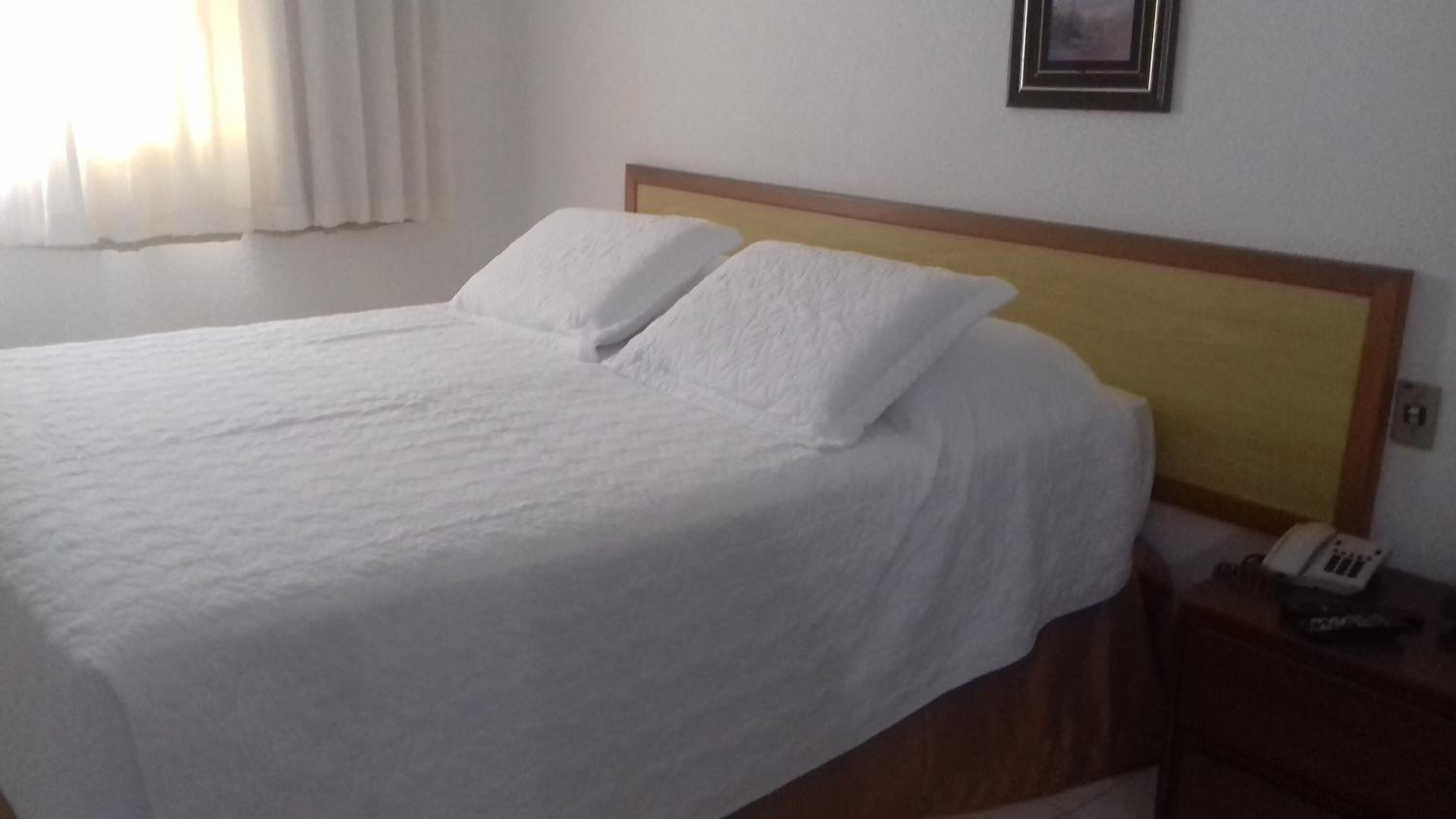 A neatly made bed with white linens in a hotel room.