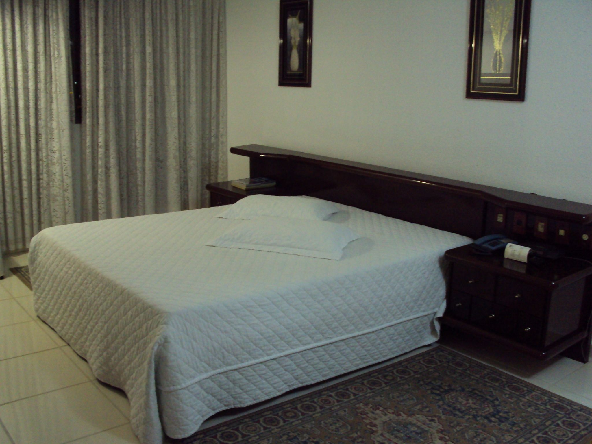 A neatly made bed with pillows, a bedside table with a lamp, and a patterned rug on the floor.