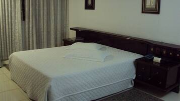 A neatly made bed with pillows, a bedside table with a lamp, and a patterned rug on the floor.