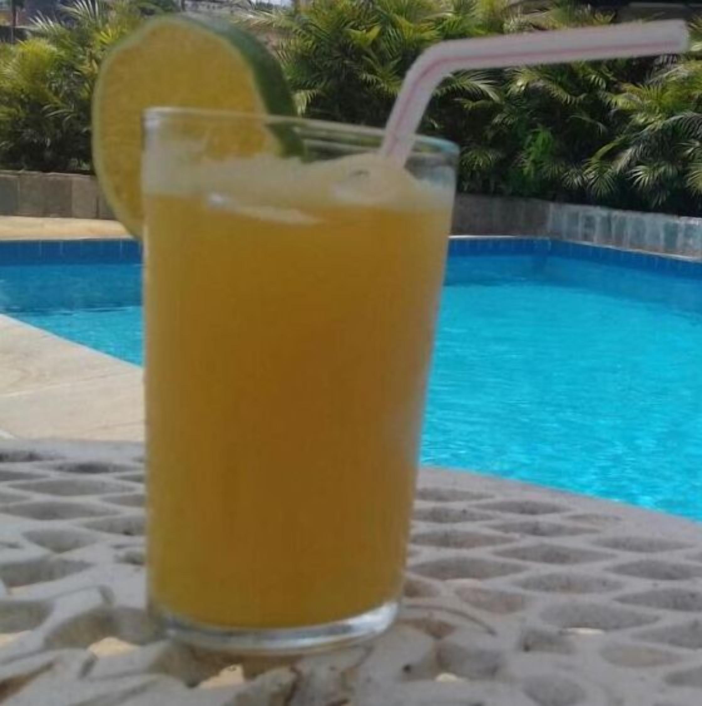 A glass of orange juice with a straw and a lime slice on a table by a pool.