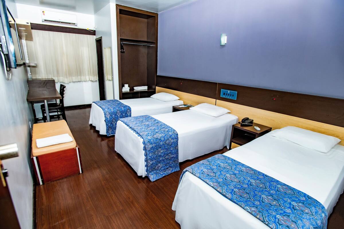 A hotel room with two beds, a desk, a chair, a wardrobe, and a small table.