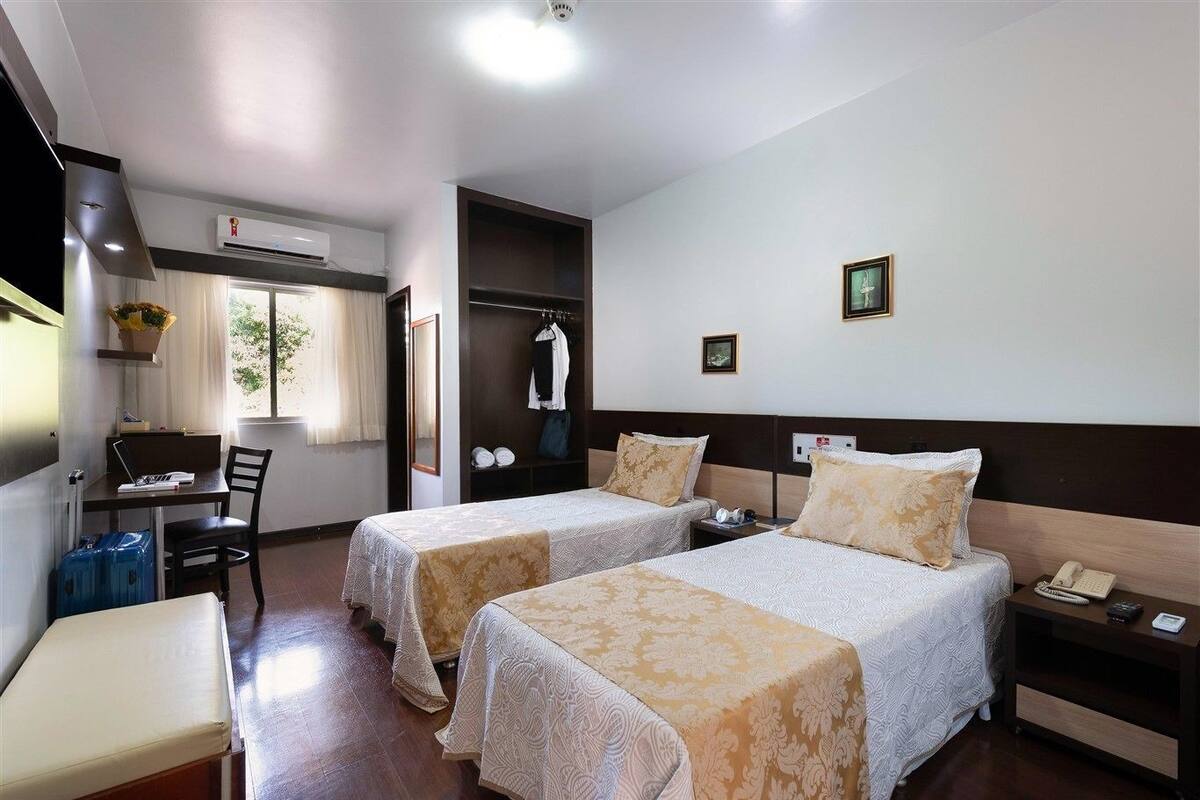 A hotel room with two beds, a desk, a chair, a wardrobe, and a small window.
