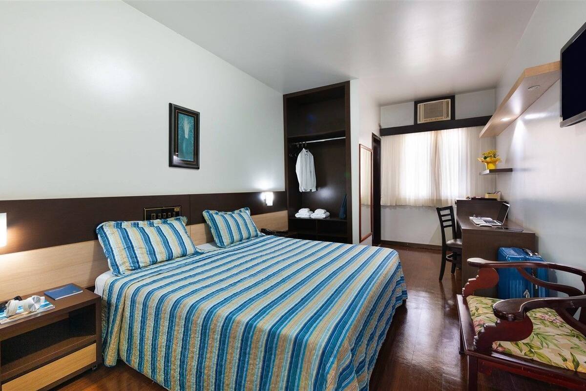 A hotel room with a bed, bedside table, chair, desk, and a TV.