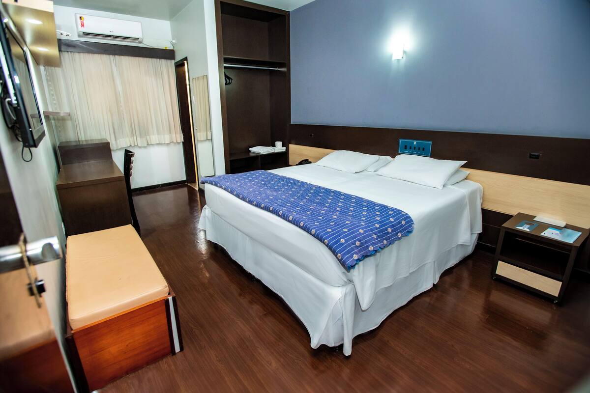 A hotel room with a bed, bedside table, and a wardrobe.