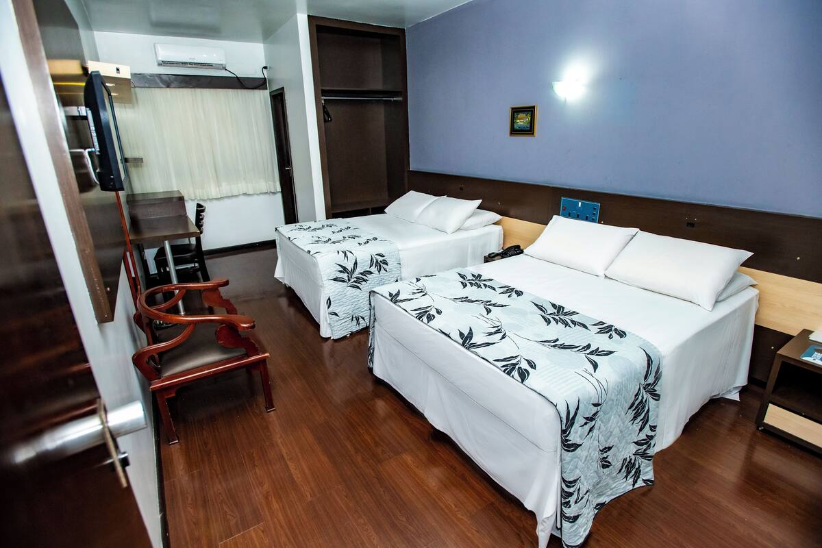 A hotel room with two beds, a wooden chair, a desk, and a wardrobe.