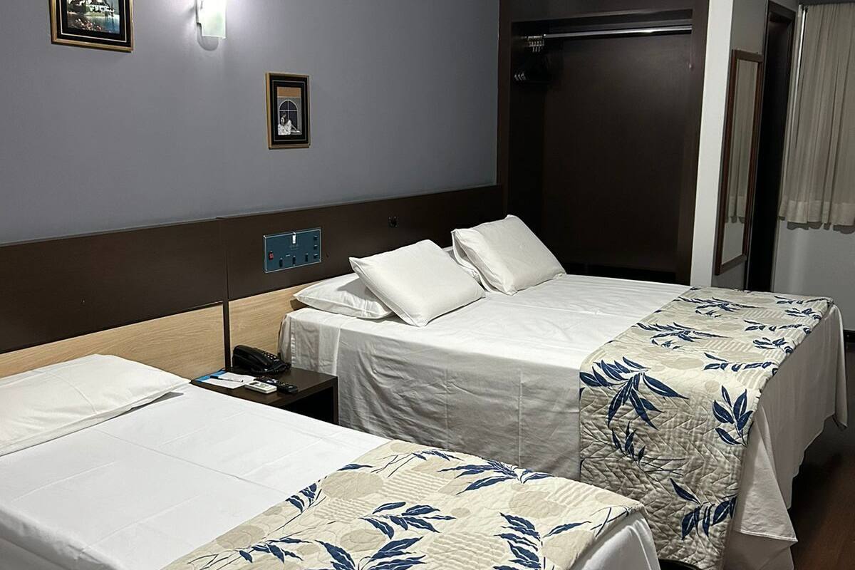 A hotel room with two single beds, a wooden headboard, a nightstand, a wall-mounted light, and a door with a curtain.