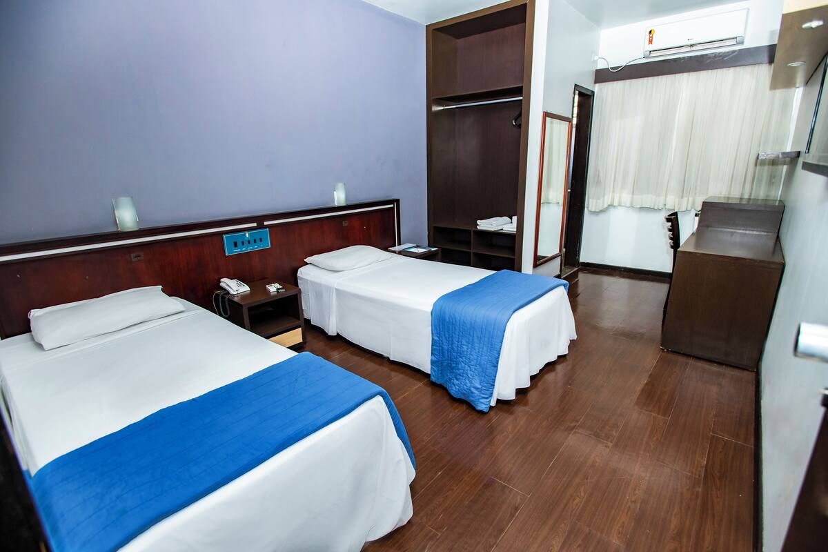 A hotel room with two beds, a wardrobe, a desk with a phone, and a mirror.