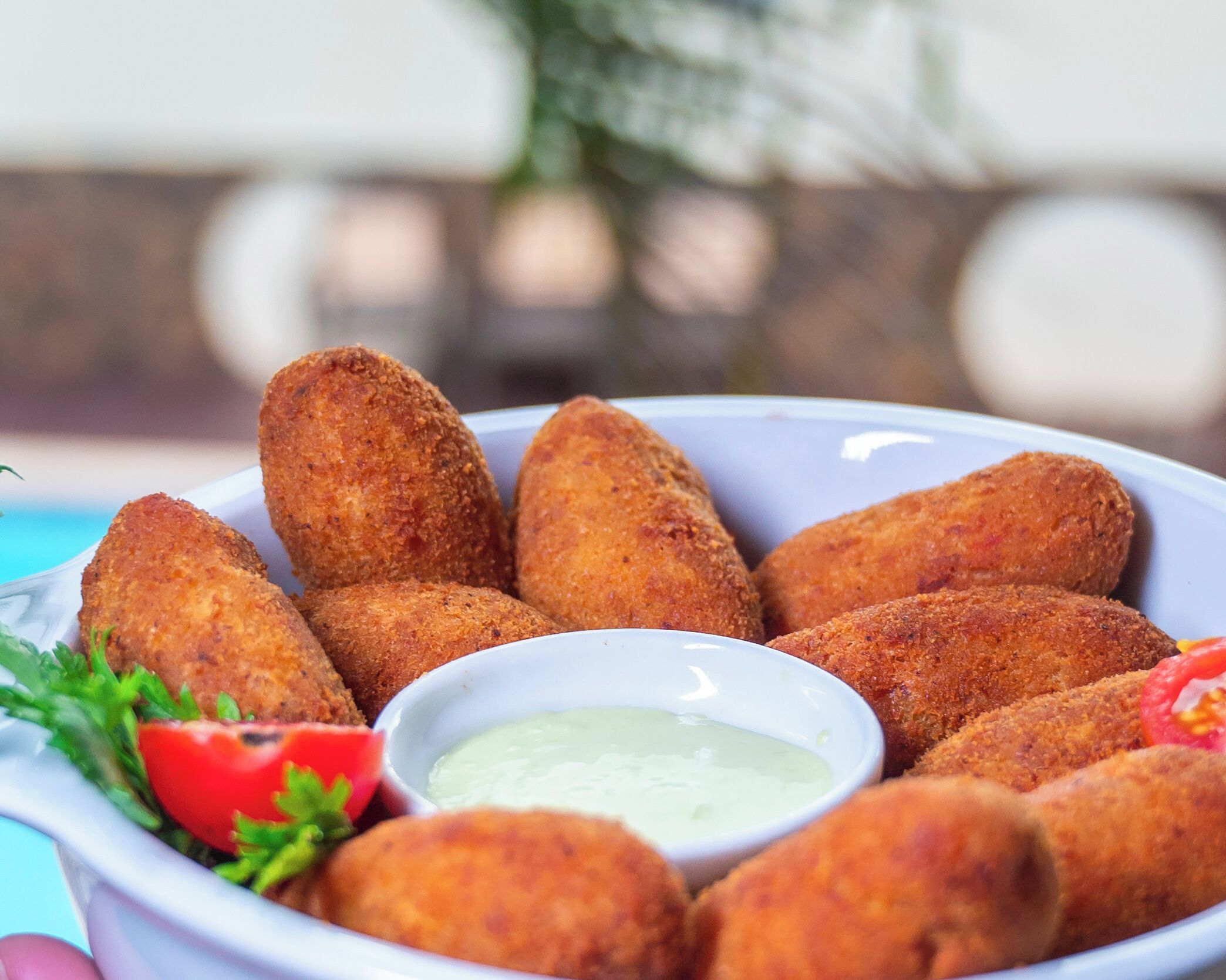 Plat de croquetes daurades amb salsa per a submergir, decorat amb un tomàquet i pernil de taronja.