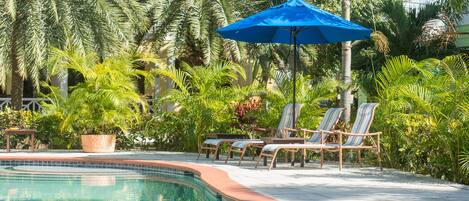 A swimming pool with lounge chairs and a blue umbrella.