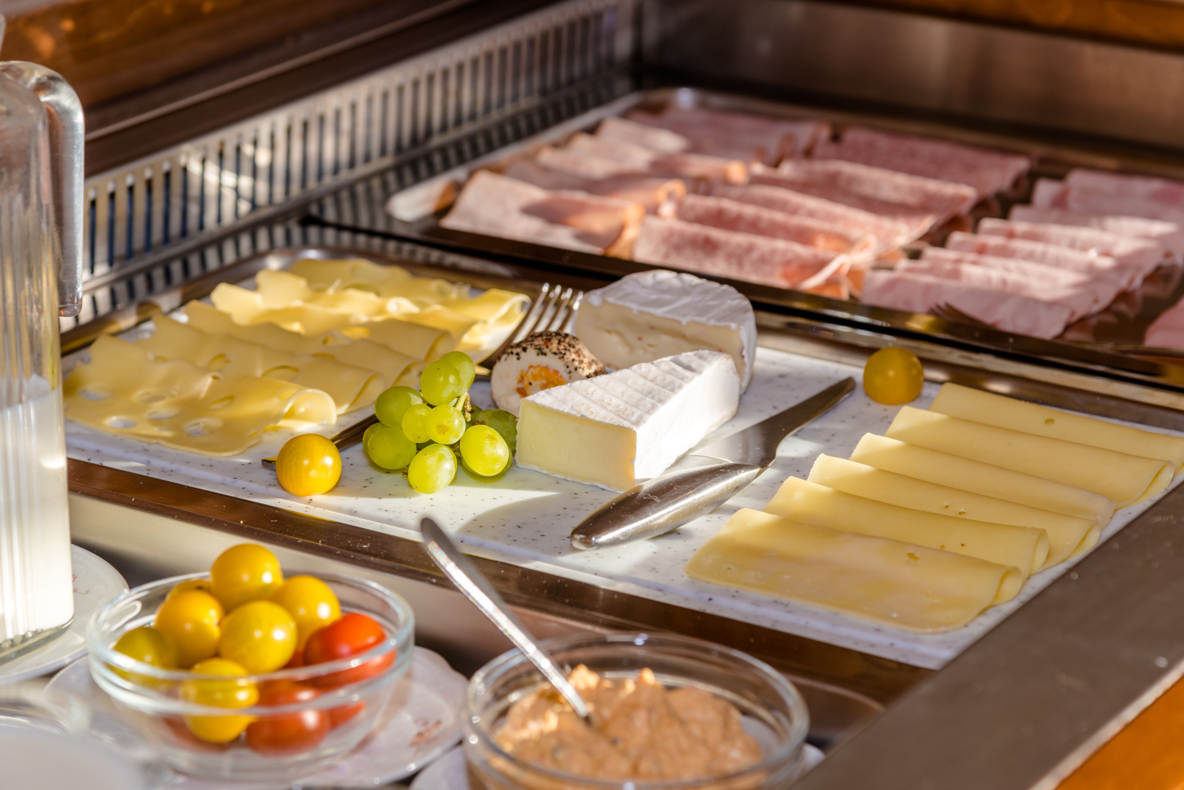 Un bufé con varios quesos, carnes y frutas.