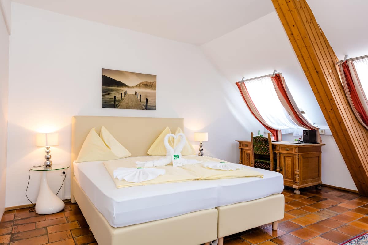 A bedroom with a bed, two bedside lamps, a painting on the wall, a wooden cabinet, and a window with curtains.