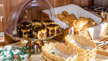 A buffet with a variety of baked goods, including cakes and pastries, displayed on a glass-covered stand and in wicker baskets.