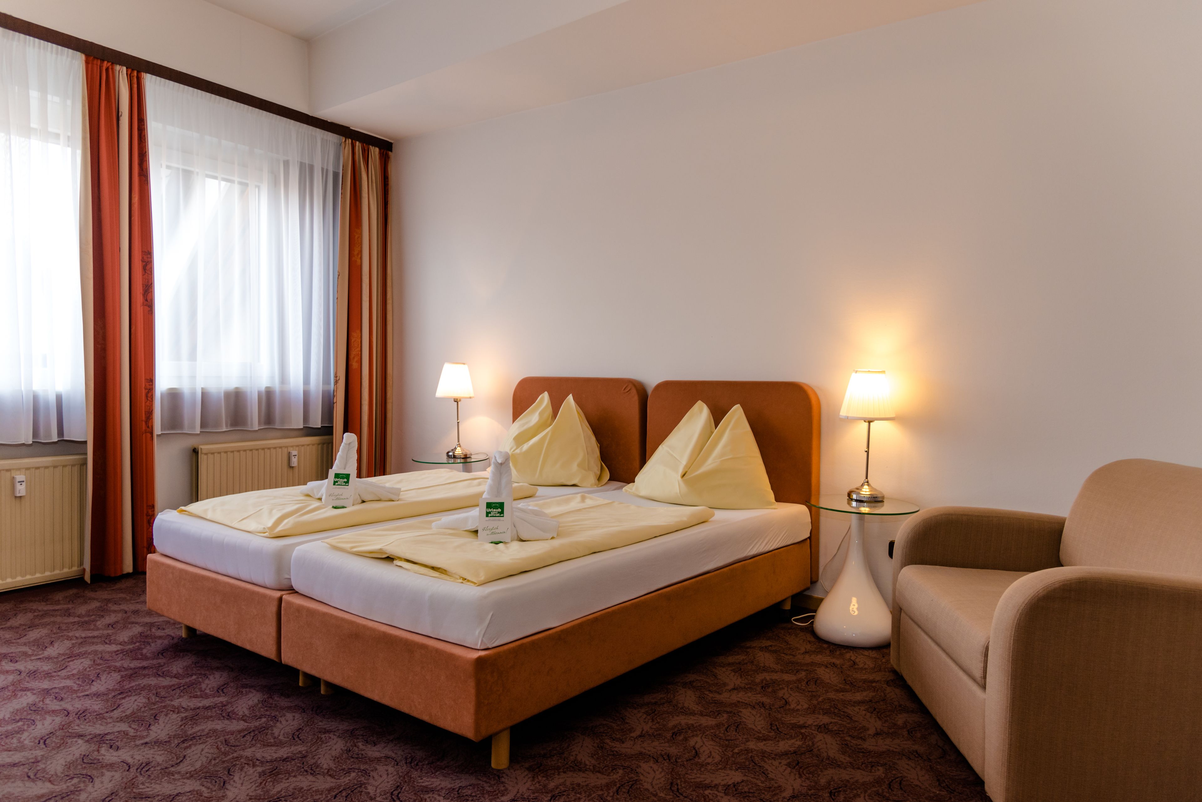 Une chambre d’hôtel avec un lit double, deux tables de chevet avec des lampes, un canapé et une fenêtre avec des rideaux.