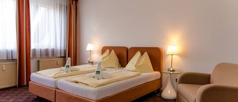 Une chambre d’hôtel avec un lit double, deux tables de chevet avec des lampes, un canapé et une fenêtre avec des rideaux.