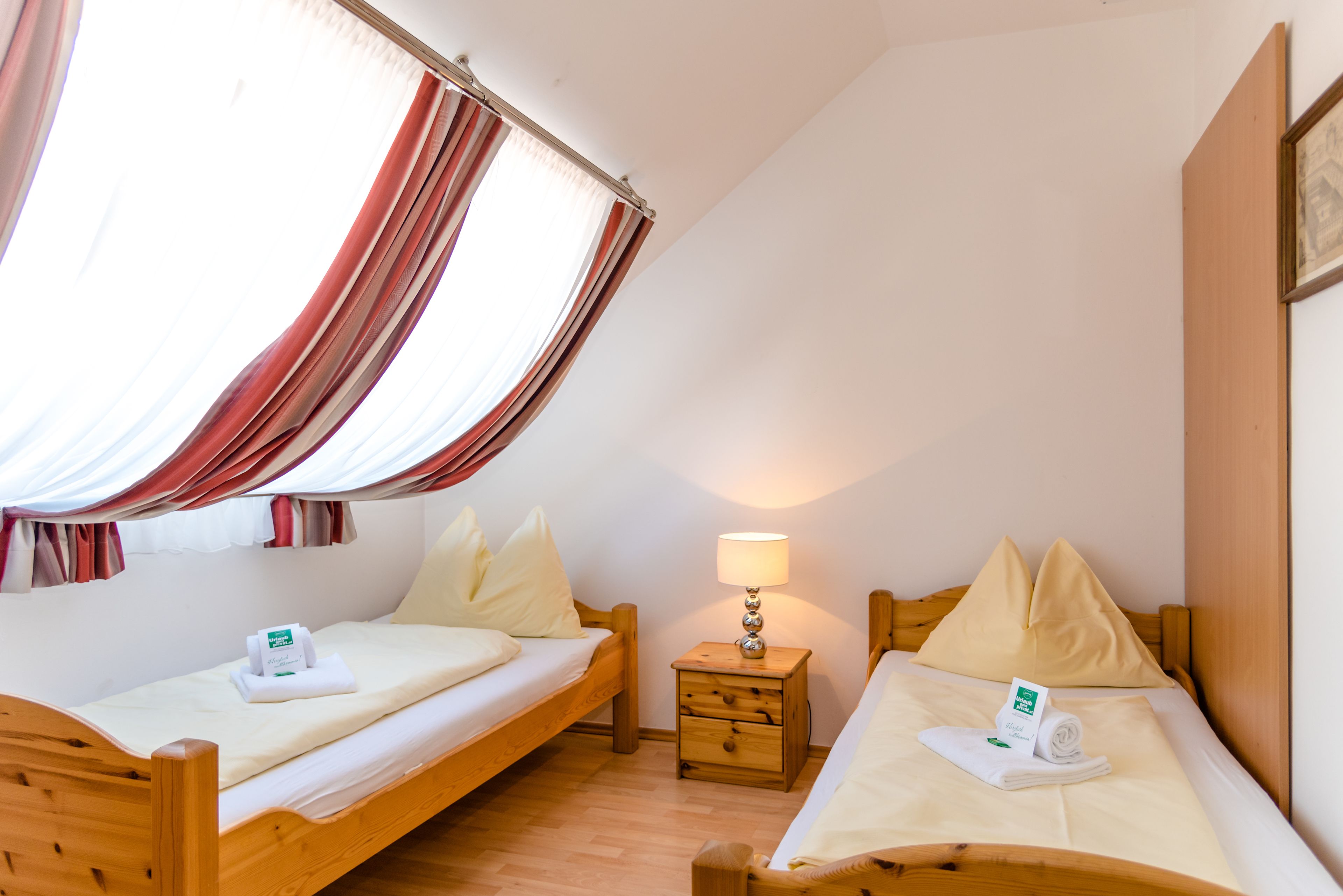 A room with two wooden beds, a nightstand with a lamp, and a window with curtains.