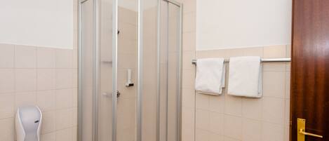 A shower enclosure with a glass door, a towel rack with two white towels, and a paper towel dispenser.